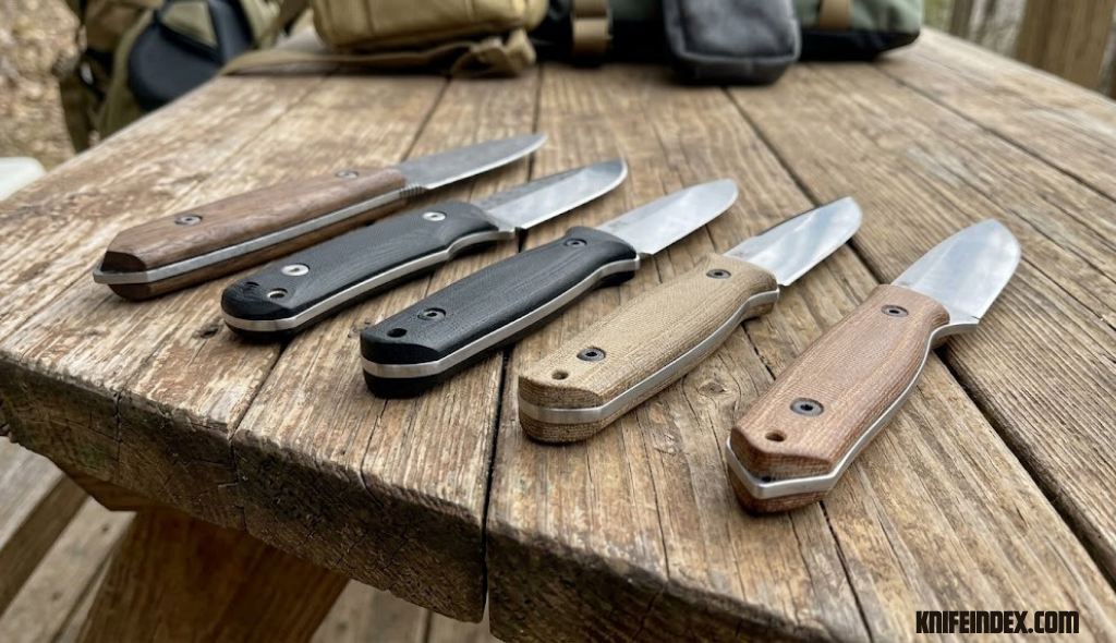 Row of fixed blade knives showing exposed steel tangs on wooden table